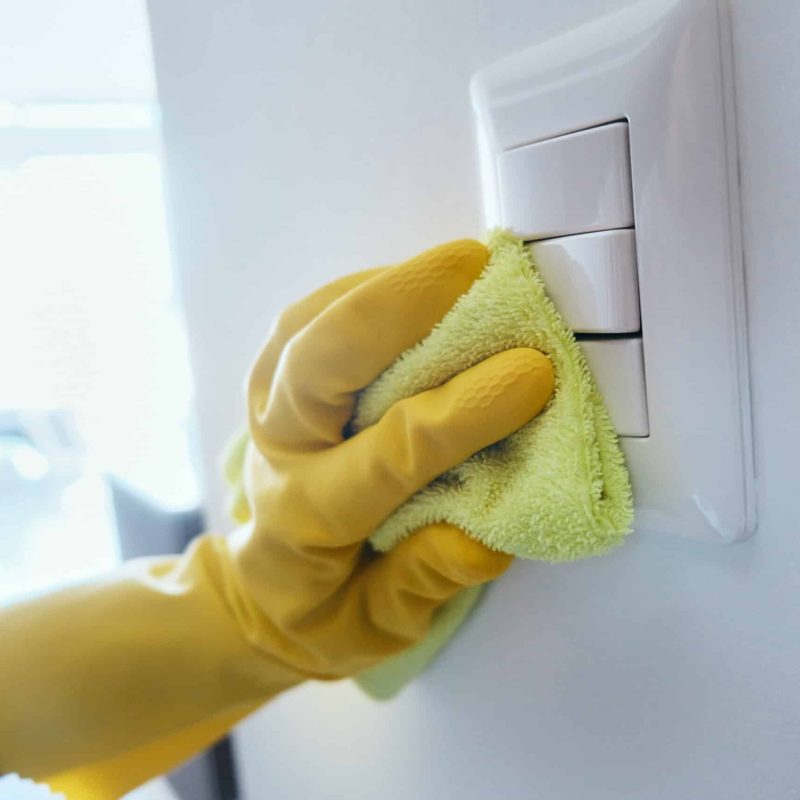 Close up view of person wiping electrical and light switches at home. People cleaning and disinfecting domestic surfaces to prevent virus and bacteria spread.