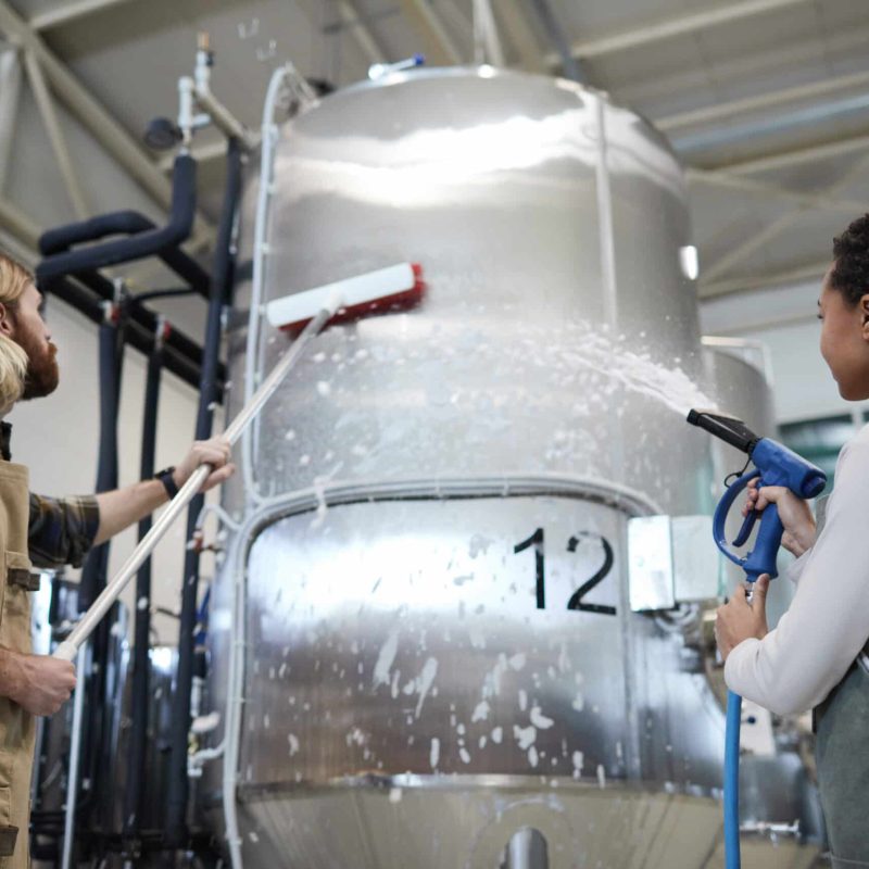 Low angle view at two workers washing equipment at modern industrial brewery, copy space